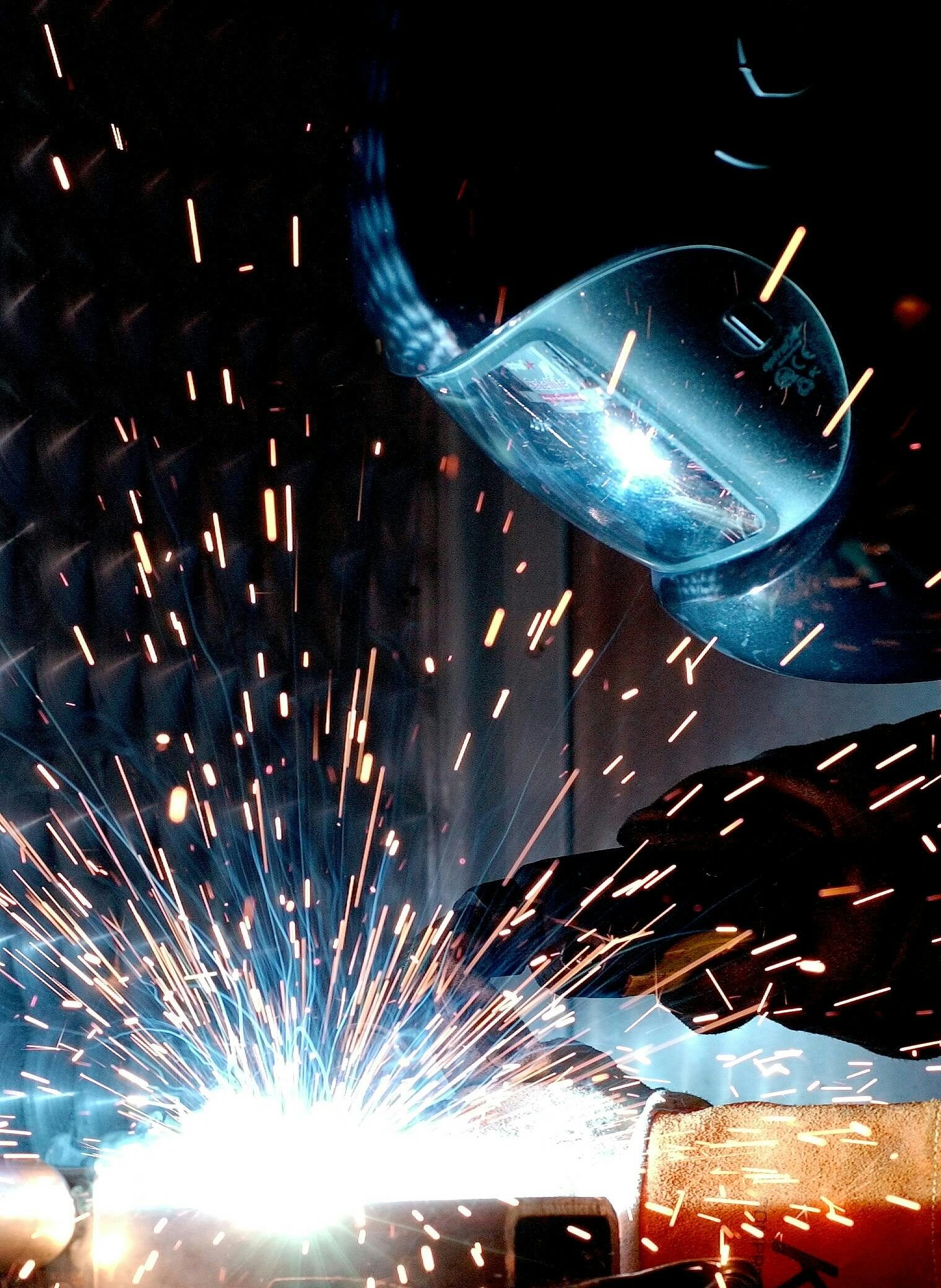 A focused welder works with metal in an industrial setting, creating vibrant sparks.